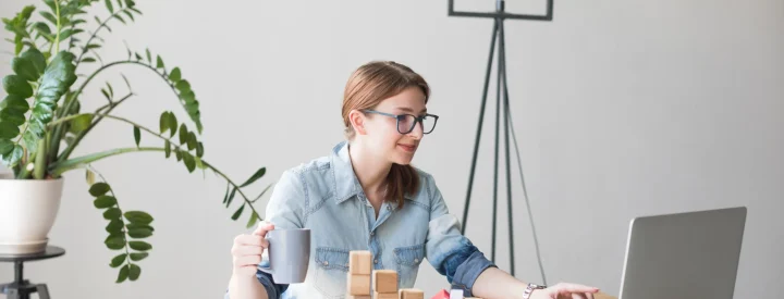 smiling-attractive-woman-holding-coffee-cup-while-working-laptop