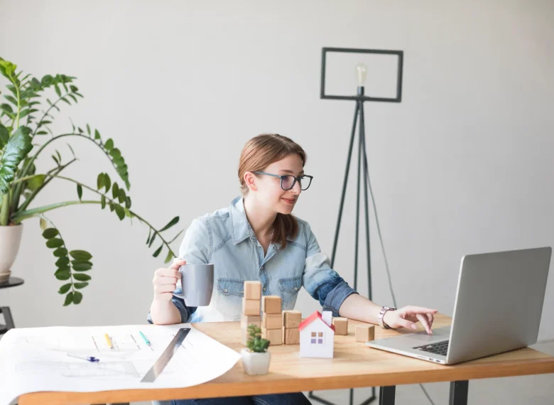 smiling-attractive-woman-holding-coffee-cup-while-working-laptop